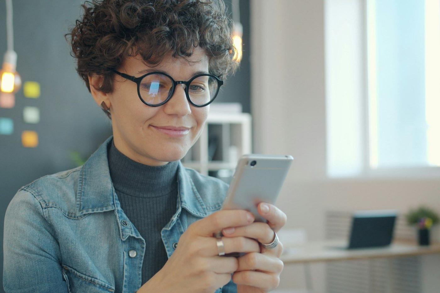 Woman with glasses smiling while using a smartphone