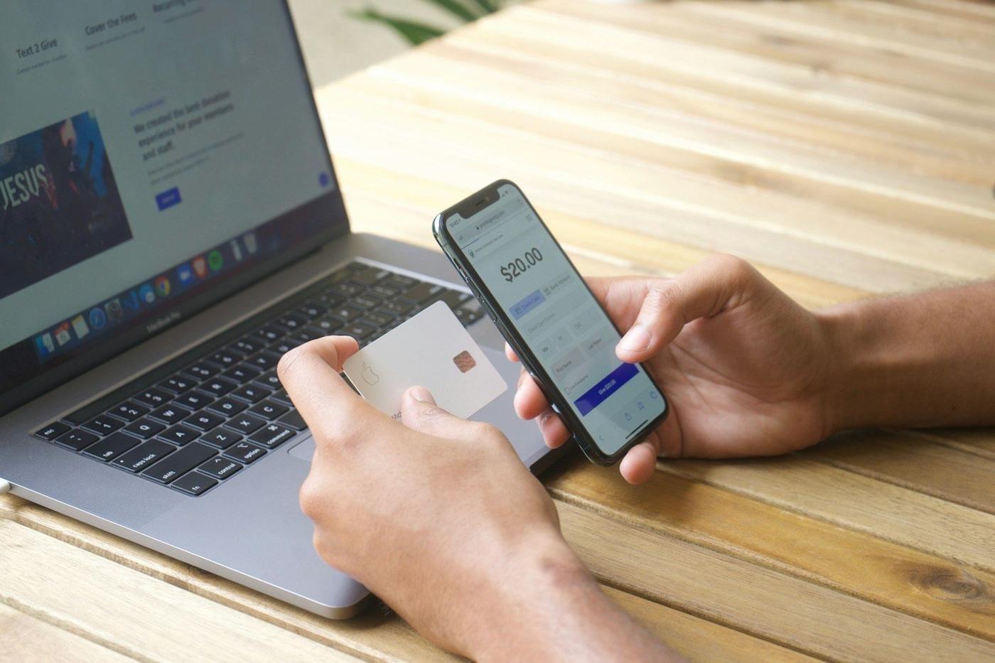 Person holding a credit card and smartphone in front of a laptop