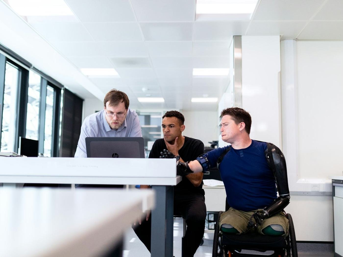 Man using a wheelchair working at an office desk with colleagues and laptops