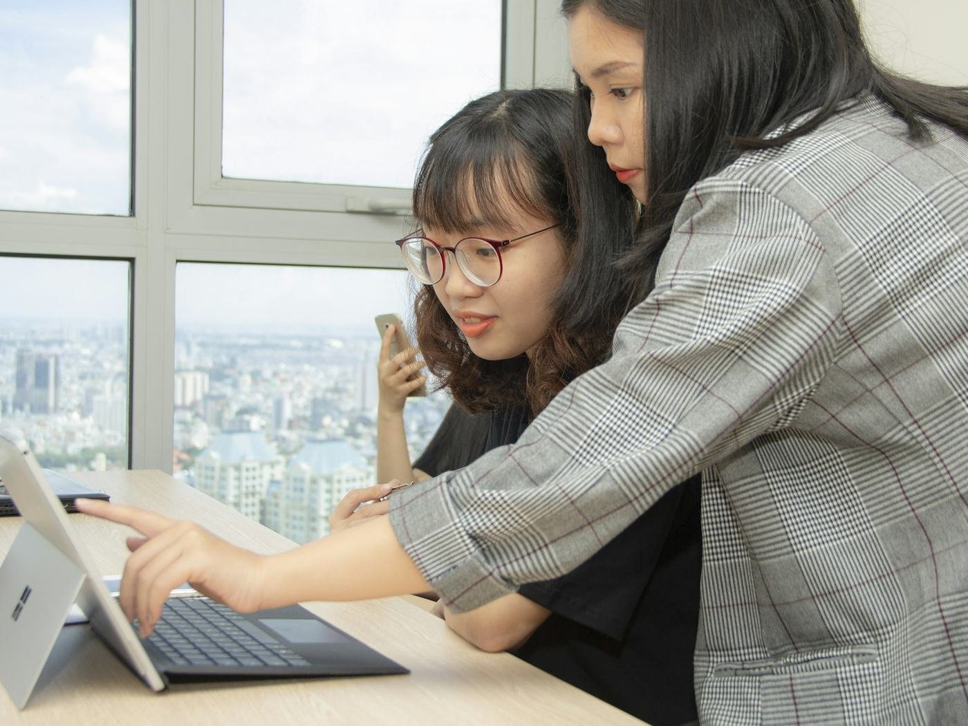 Woman leaning over a seated colleague and pointing at her laptop screen