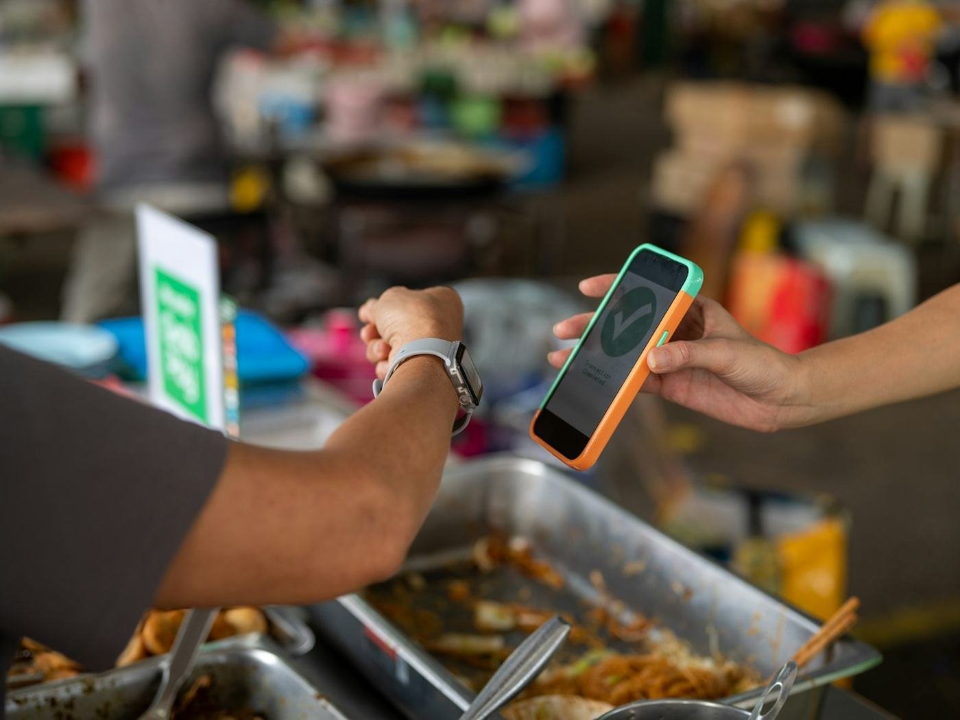 Customer holding out a smartphone to pay at a Southeast Asian street food stall