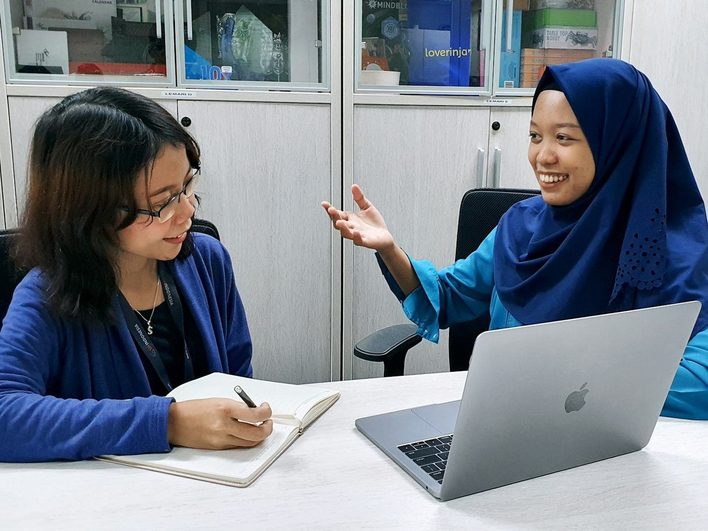 Researcher taking notes while a participant in a hijab talks during a laptop-based user session
