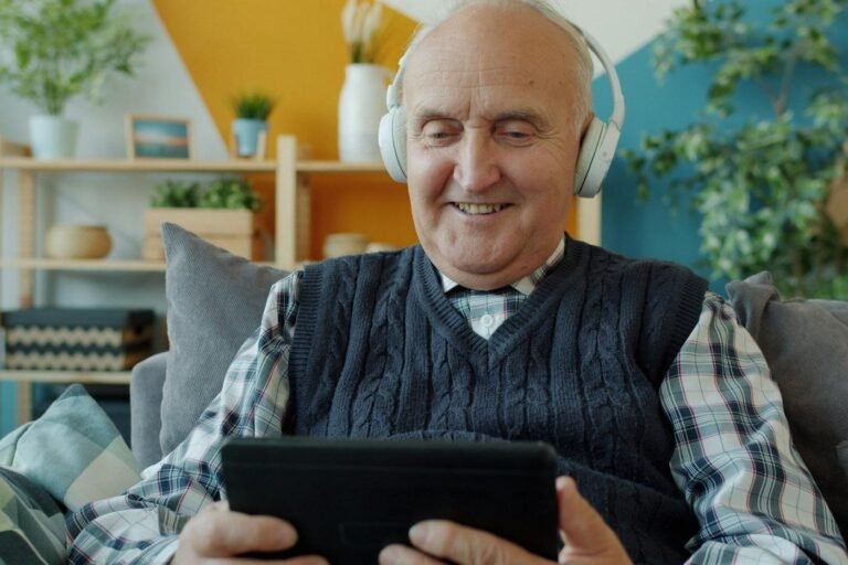 Older man wearing headphones using a tablet on a sofa