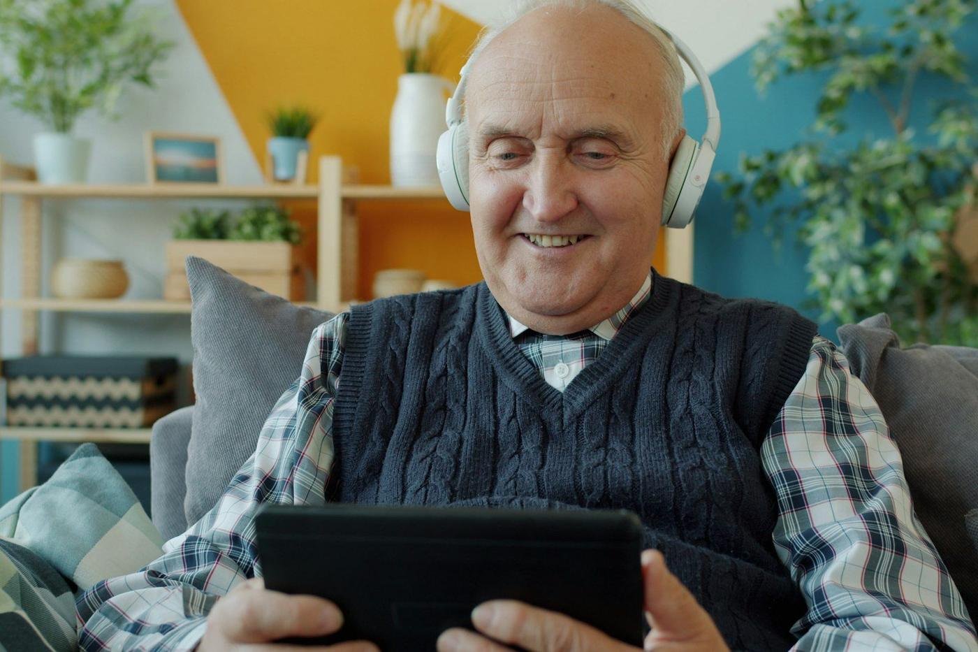 Older man wearing headphones using a tablet on a sofa