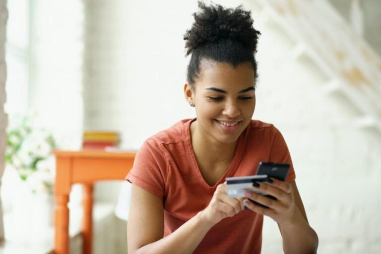 Young woman smiling while holding a credit card and smartphone