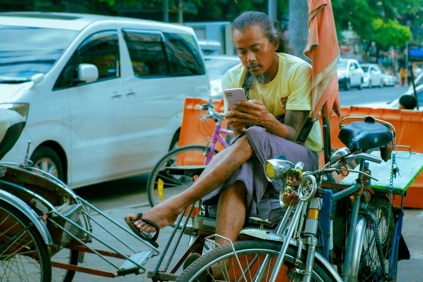 Man sitting in a cycle rickshaw using his phone on a city street