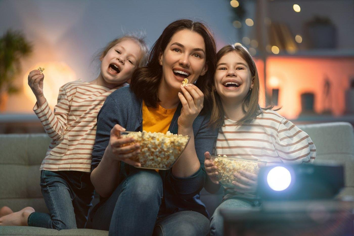 Woman and two children eating popcorn while watching a movie at home