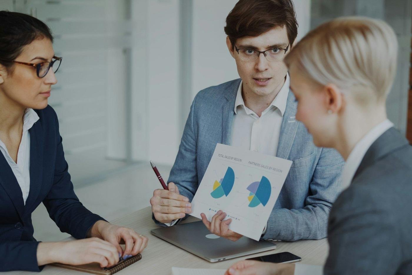 Three professionals reviewing printed charts in a meeting