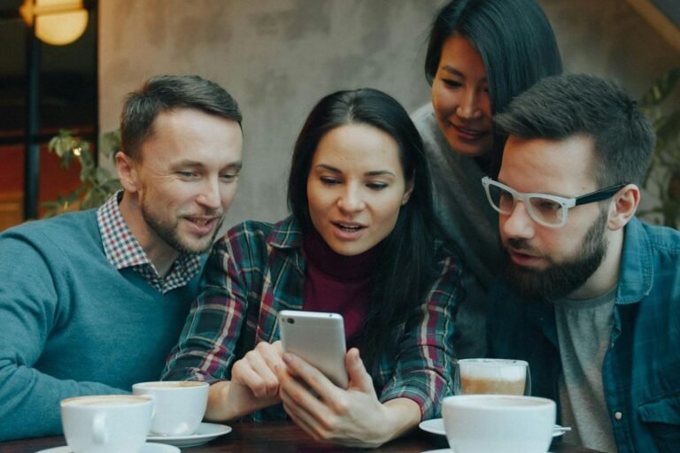 Four people in a cafe gathered around a smartphone